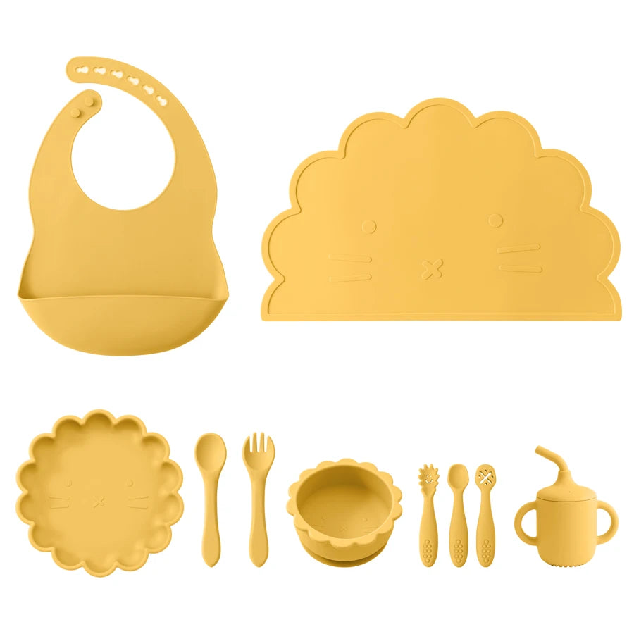Yellow silicone baby feeding set including bib, placemat, plates, utensils, and cup on a white background