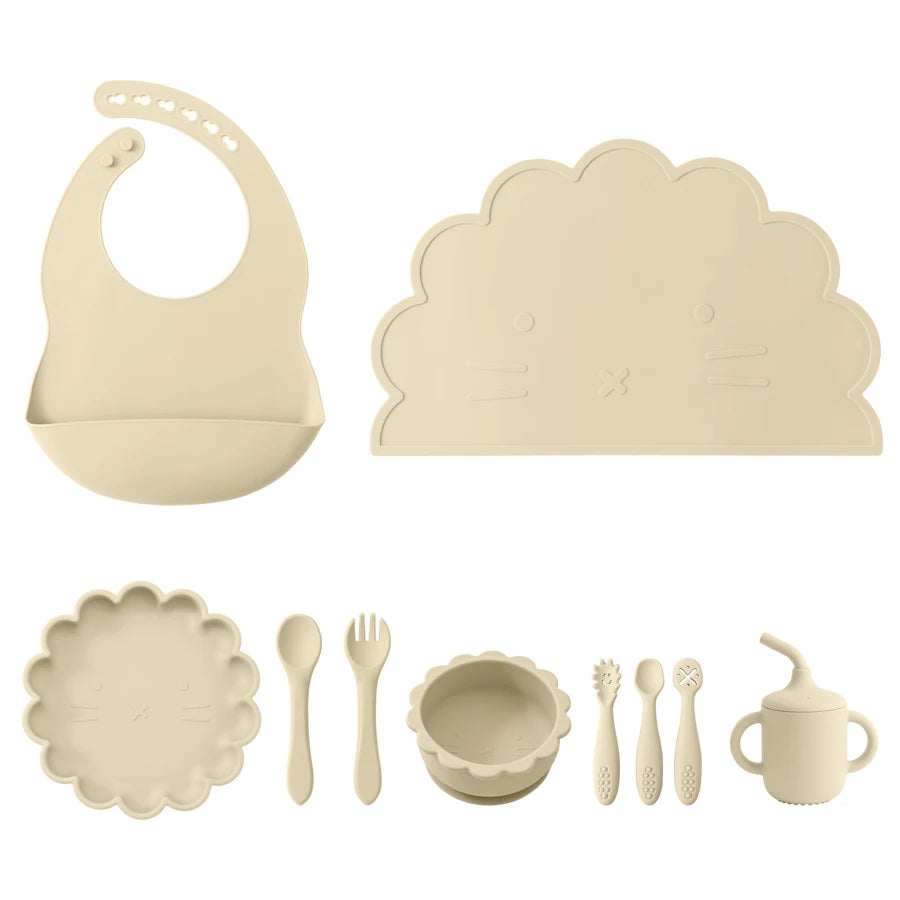 Beige baby dining set with bib, plate, bowl, and utensils on a white background
