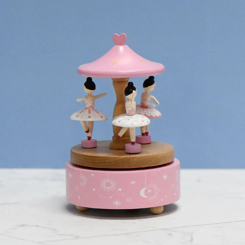 Pink carousel toy with ballerina figures on a white surface and blue background