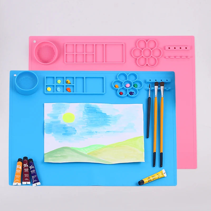 Two silicone mats, one blue and one pink, with painting tools and a child's drawing on a light gray background.