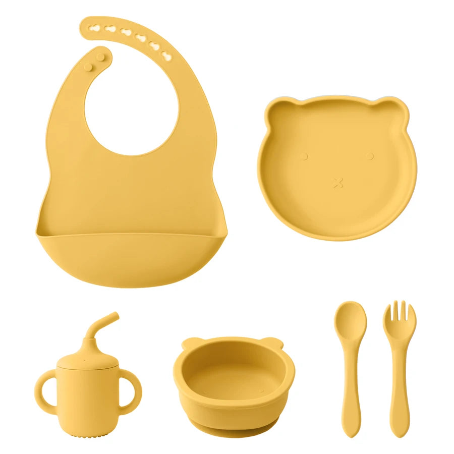 Yellow silicone baby feeding set including bib, plate, cup, bowl, spoon, and fork on a white background.