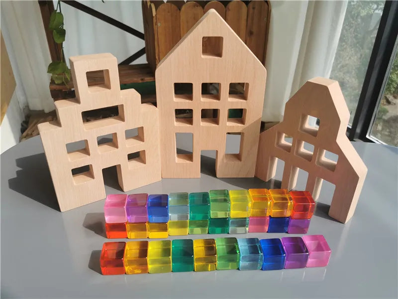 Wooden house models with colorful transparent blocks on a reflective surface.