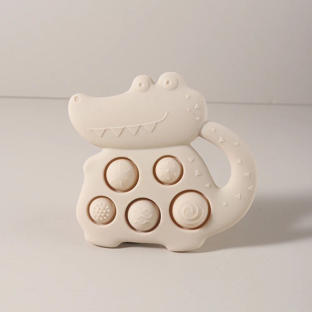 White crocodile-shaped teething toy with various textures on a light gray background