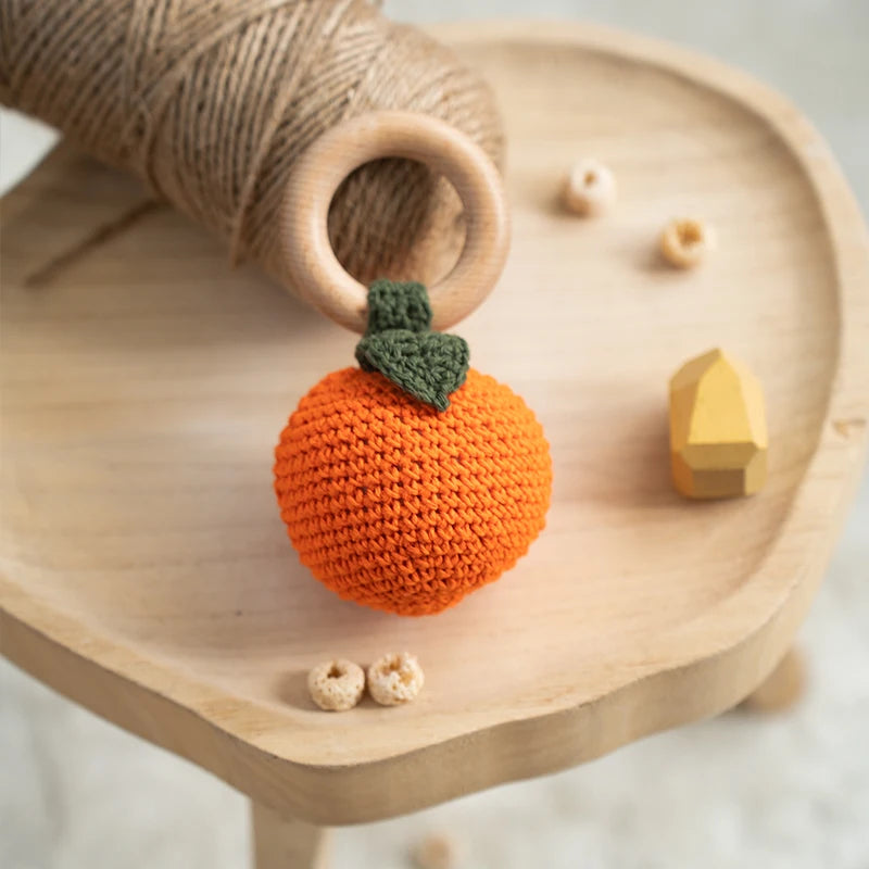 Crocheted orange pumpkin toy on a wooden surface with other toys.