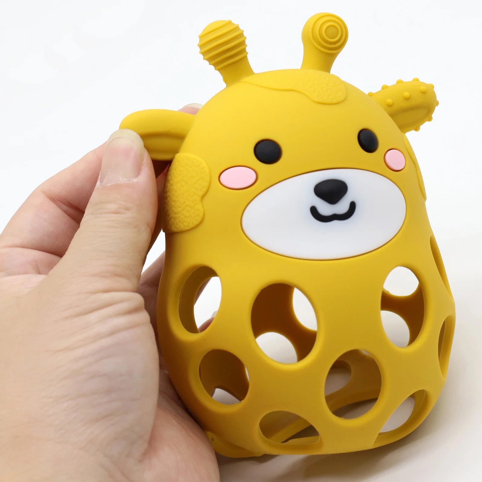Yellow giraffe-shaped silicone teething toy held by a hand on a white background