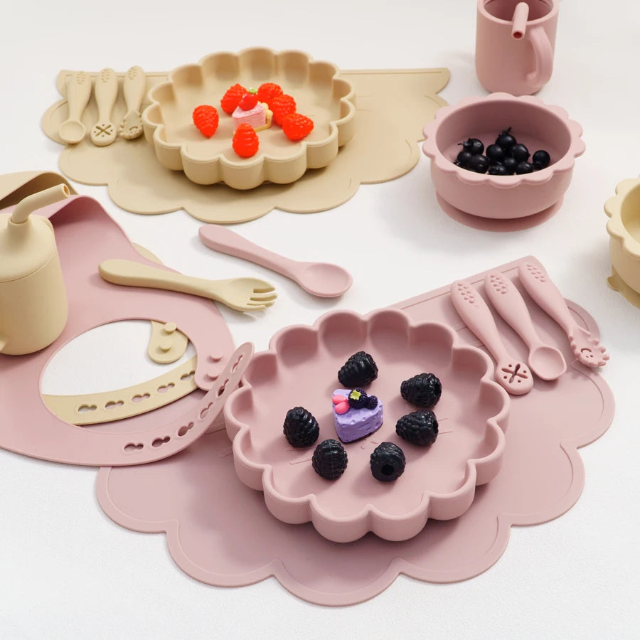 Children's tableware set with pink and beige plates, bowls, and utensils on a white background.
