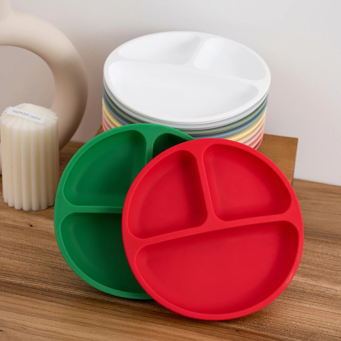 Green and red round silicone divided plates with white plates on a shelf