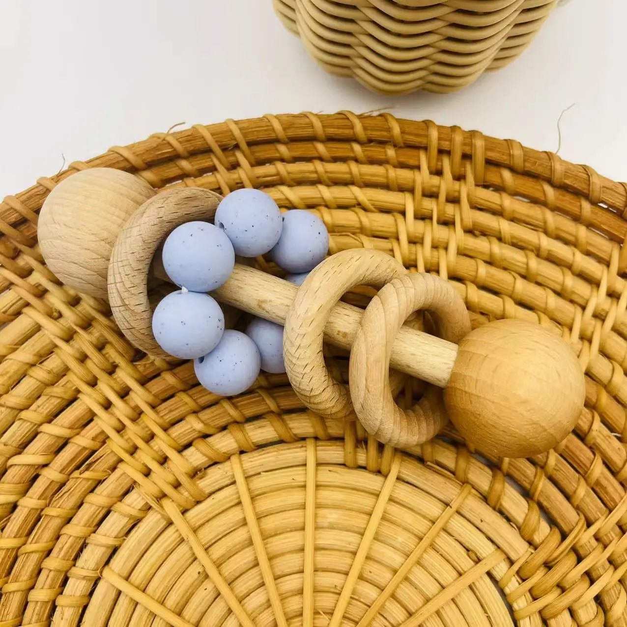 Wooden baby rattle with blue beads on a woven surface
