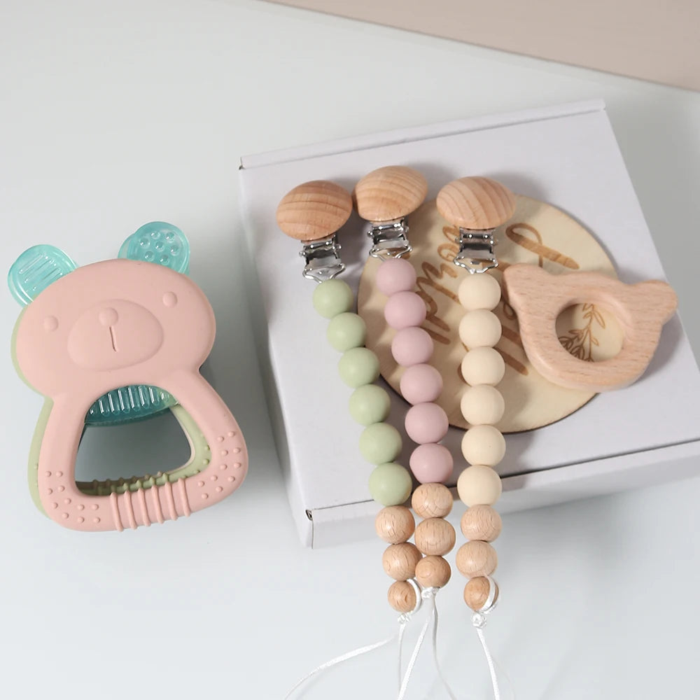 Set of baby teething toys including a pink teether, wooden beads, and a wooden toy on a white surface.