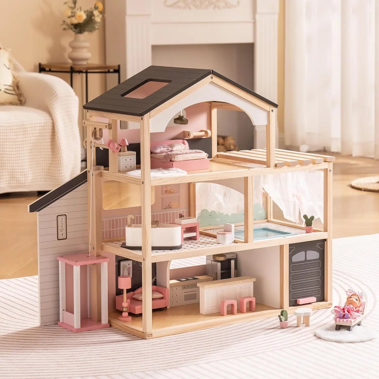 Wooden dollhouse with pink interior furniture on a light wooden floor.