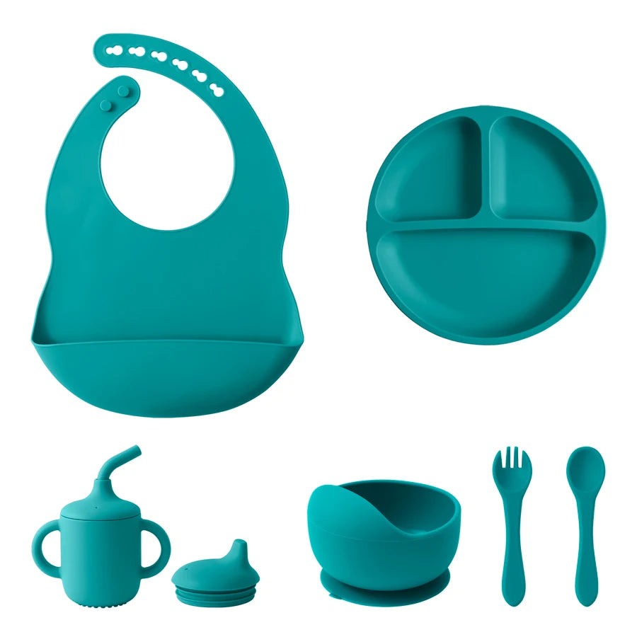 A baby feeding set in a solid teal color, including a silicone bib, a three-compartment divided plate, a sippy cup with spout and lid, a small bowl with a suction base, a fork, and a spoon, all arranged on a plain white background.