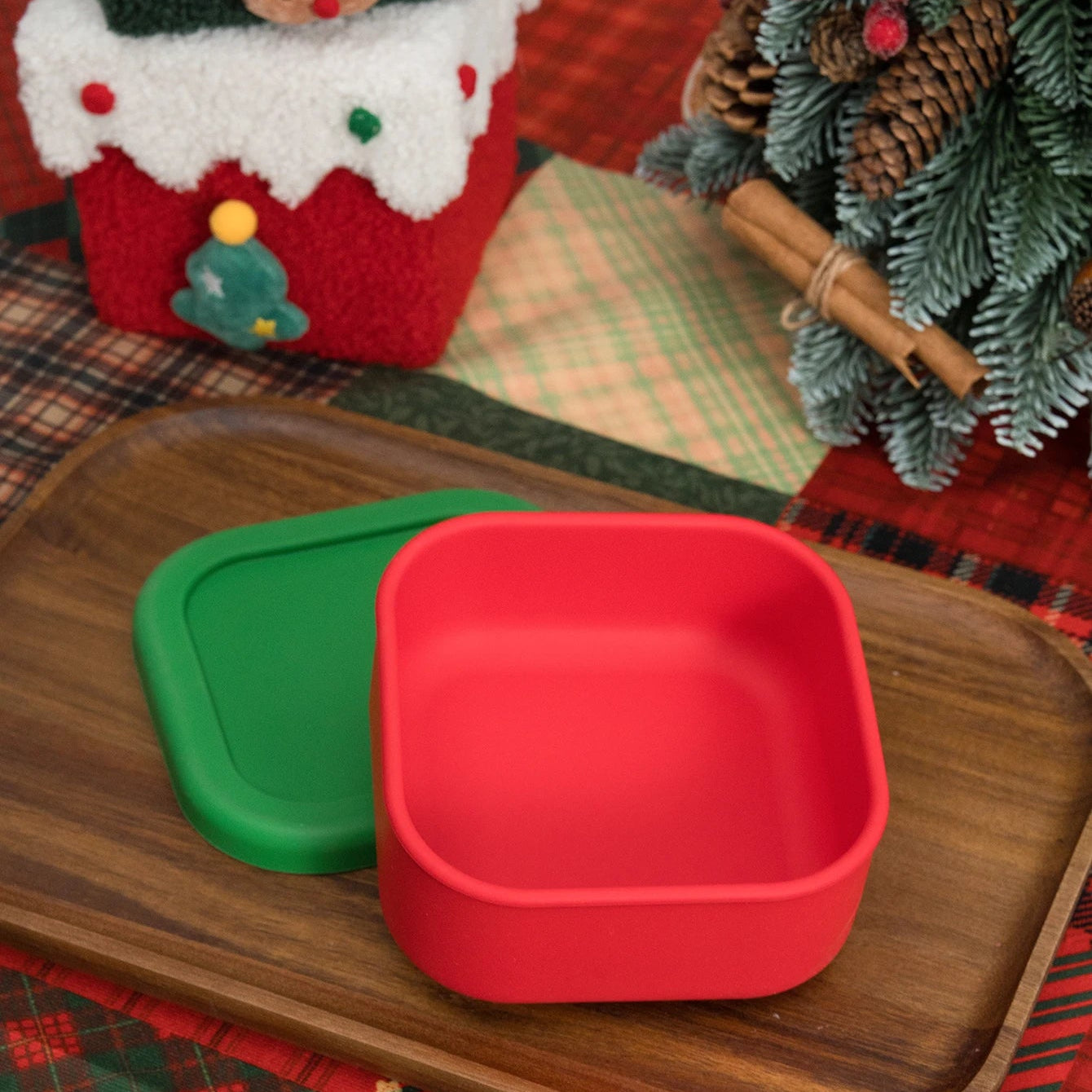 Red and green silicone snack container with lid on a wooden tray