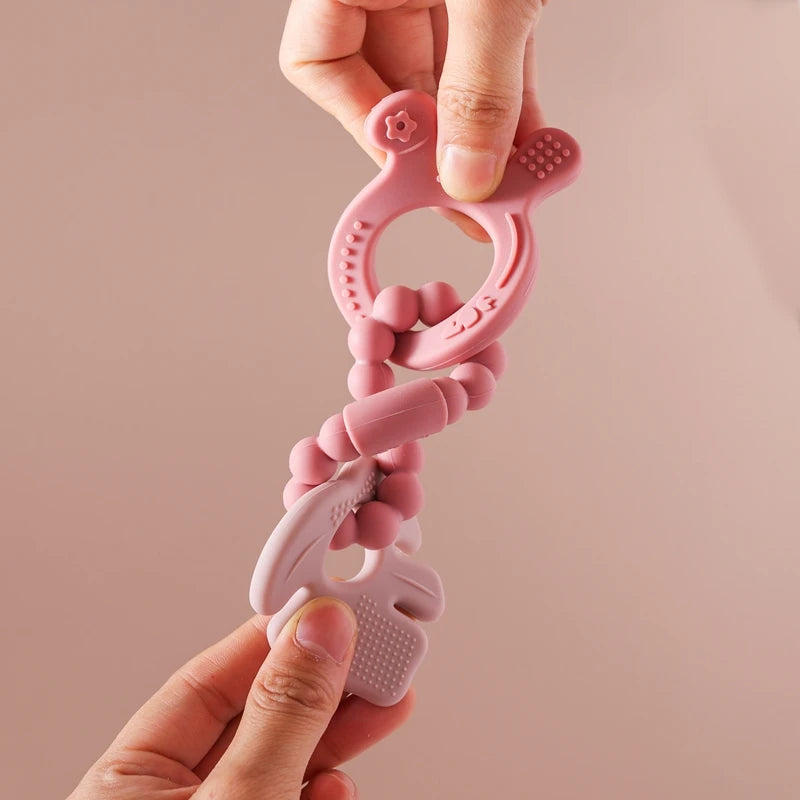 Pink baby teething ring held by a hand against a beige background