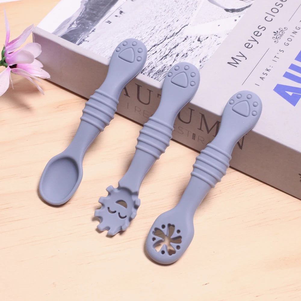 Three blue baby spoons with different designs on a light wooden surface.