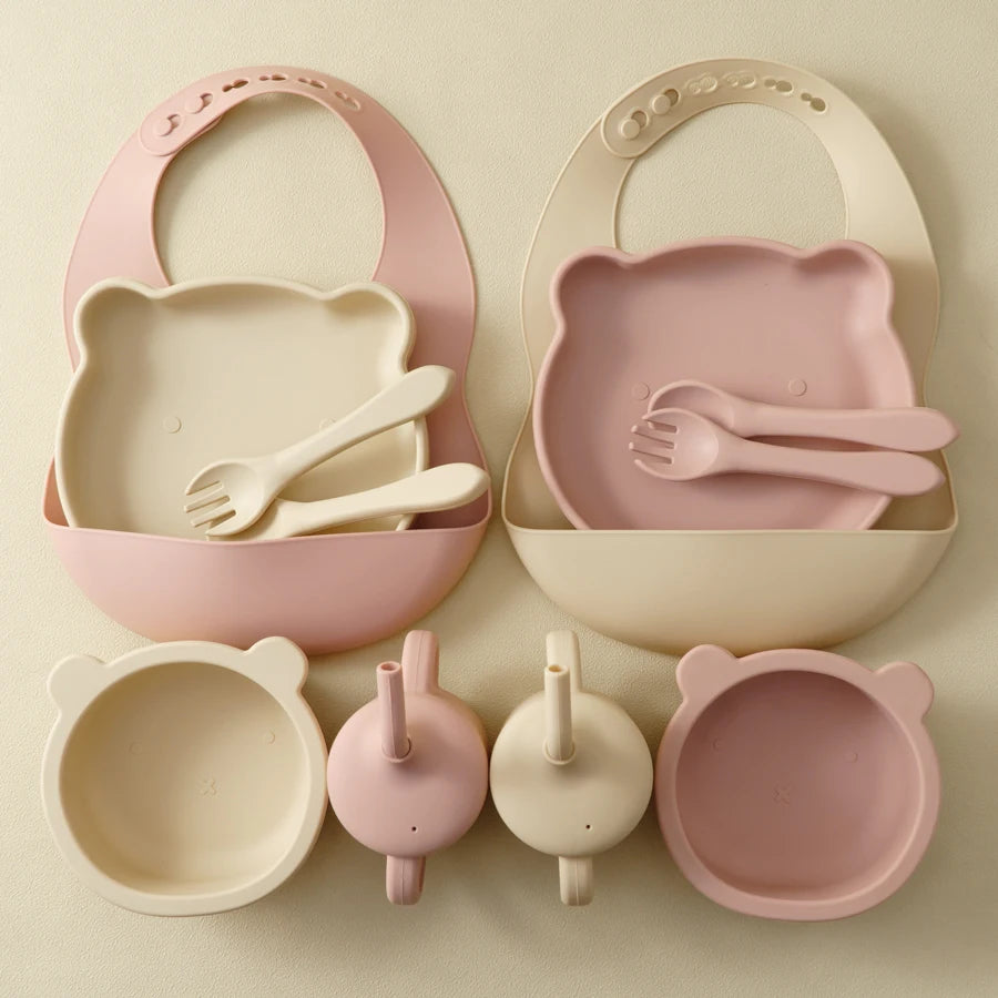Children's dining set with pink and beige bowls, spoons, and a bib on a light background