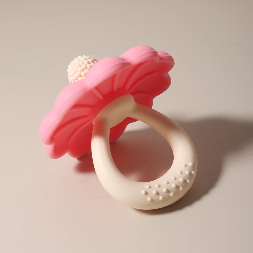 Pink flower-shaped teething ring with a white textured ring on a beige background