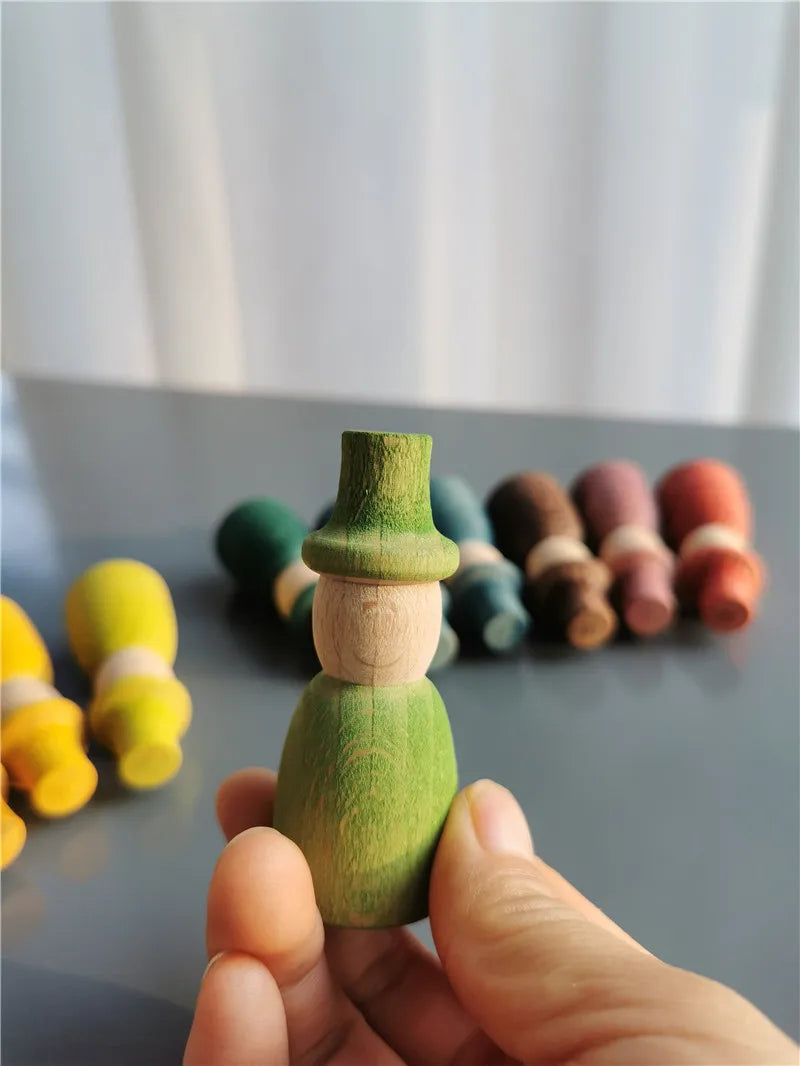 Hand holding a green wooden peg doll with others in the background on a gray surface.