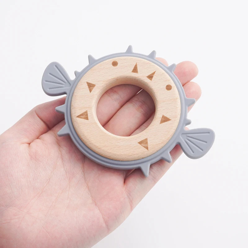 Hand holding a pebble blue pufferfish teether with wooden ring