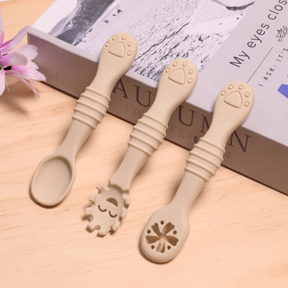 Three beige baby spoons with unique designs on a wooden surface.