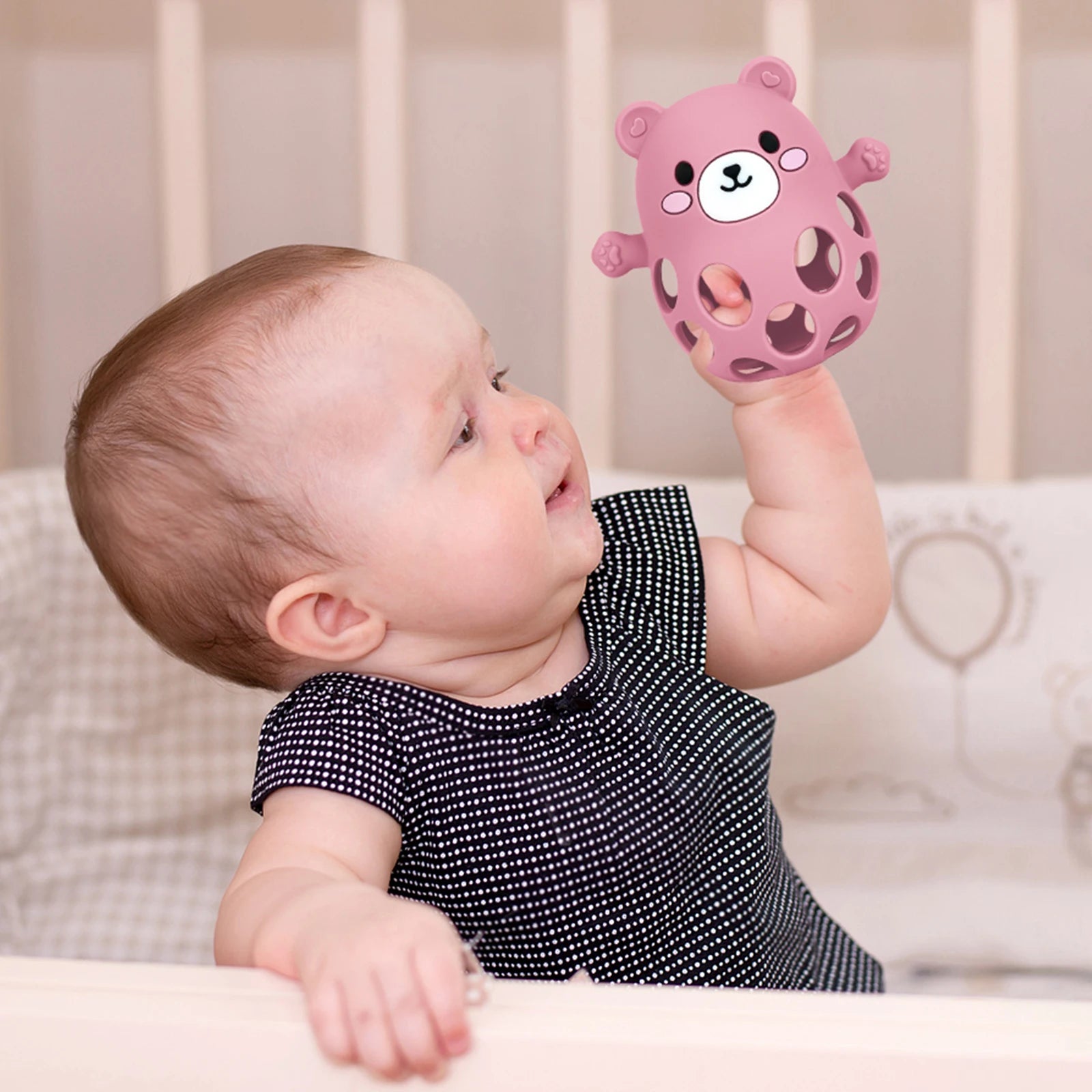Baby holding a pink bear-shaped toy in a crib