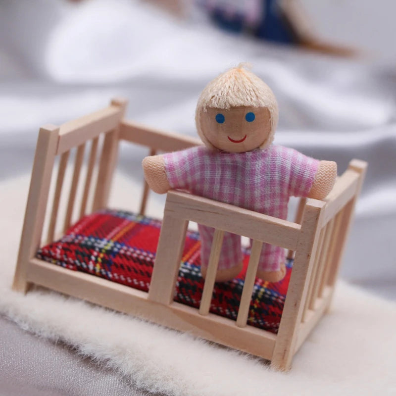 Small wooden doll with blonde hair and a pink outfit standing next to a miniature bed with colorful bedding.