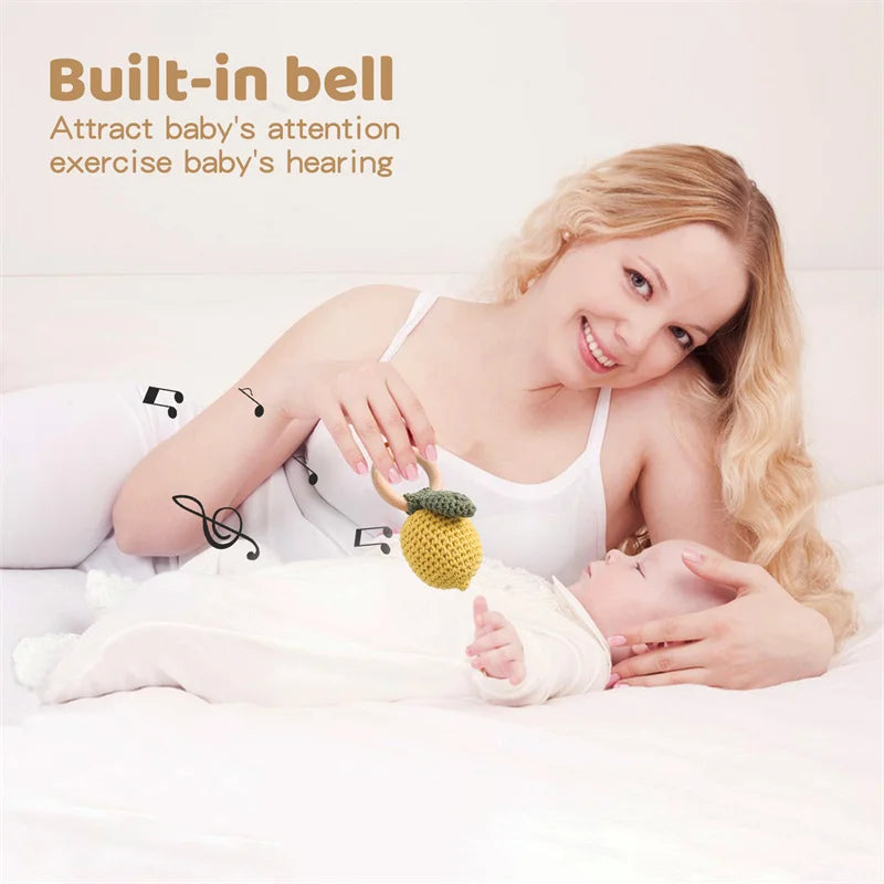 Woman holding a baby and a toy with text about a built-in bell for baby's attention and hearing.