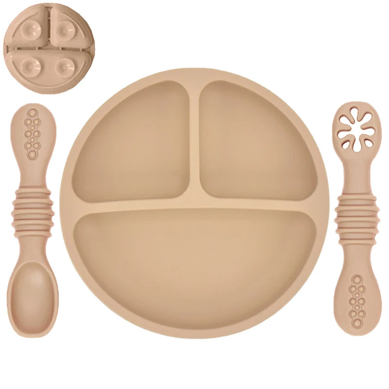 Beige silicone plate with divided sections, two spoons, and a fork on a white background