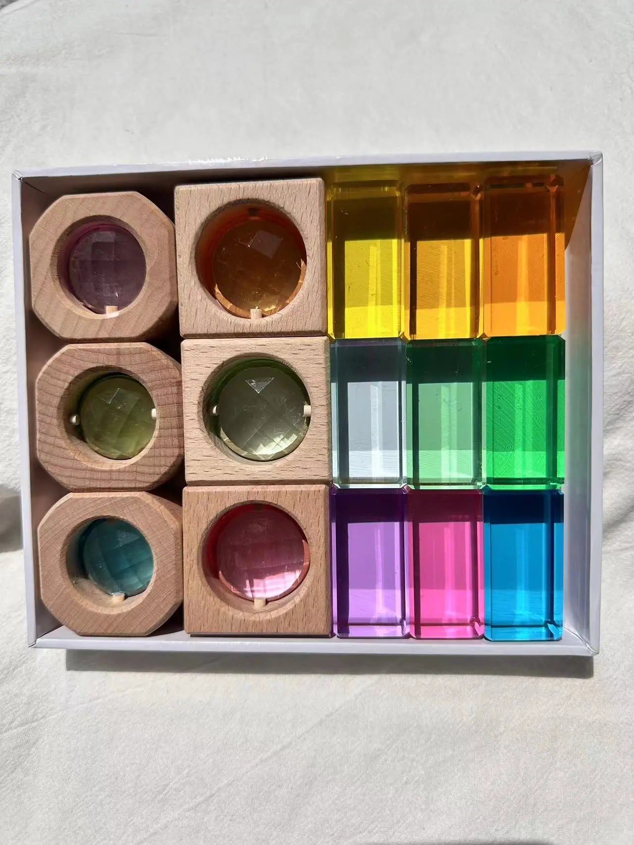 Set of wooden and transparent colorful blocks in a box on a light background