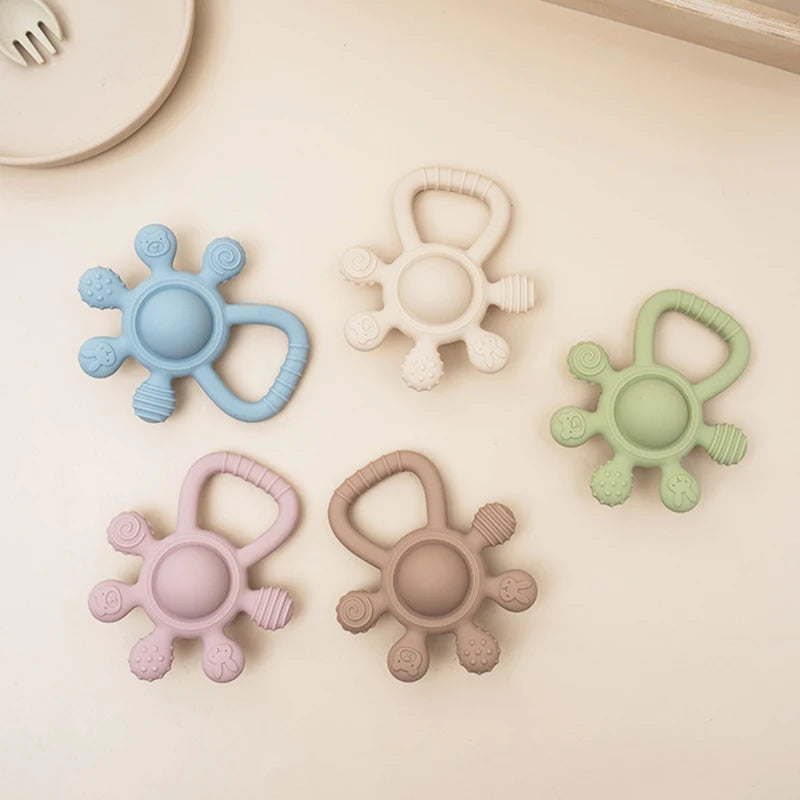 Five colorful baby teething rings on a light beige surface