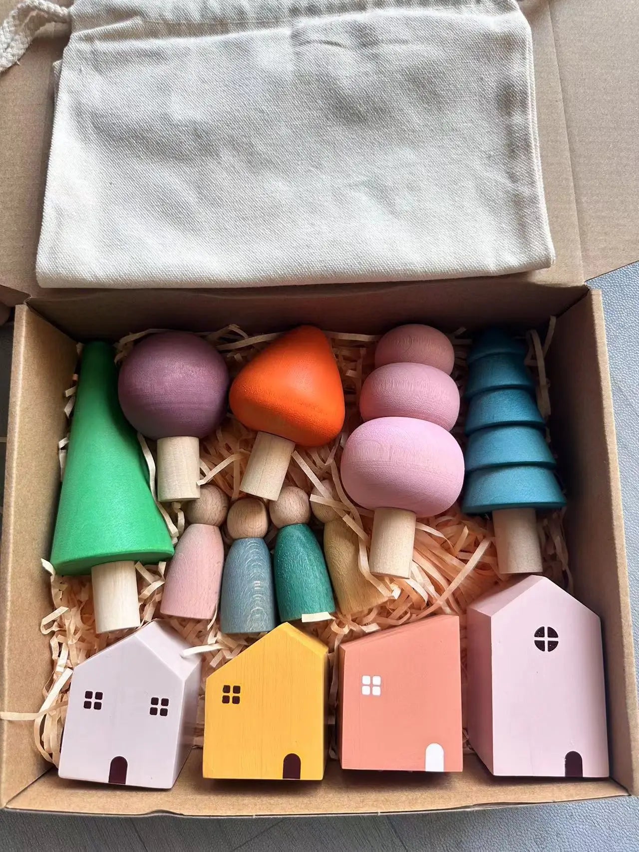 Colorful wooden toys including houses and trees in a box with a cloth cover.