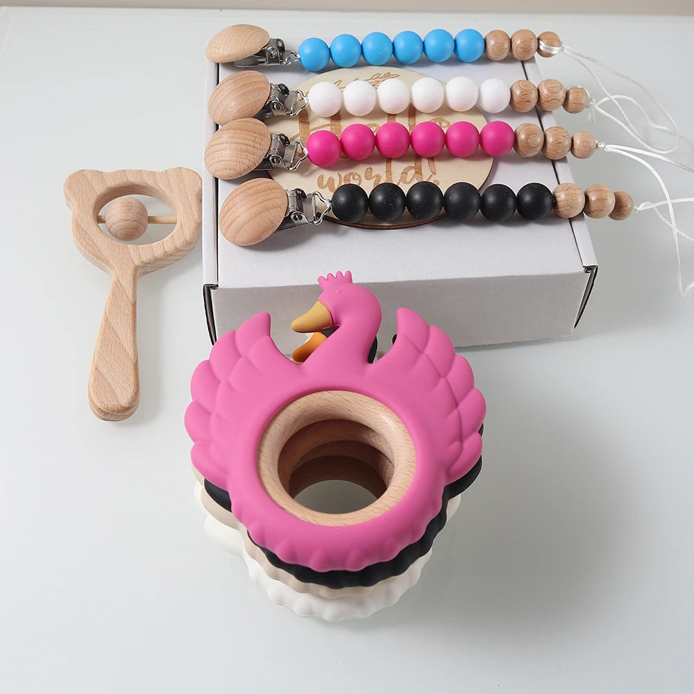 Pink swan-shaped teether with wooden rattle and pacifier clips on a white background
