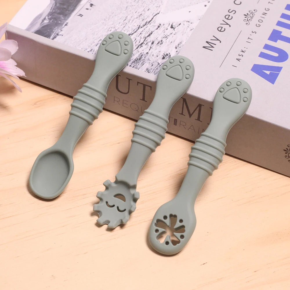 Three green baby utensils with unique designs on a wooden surface.