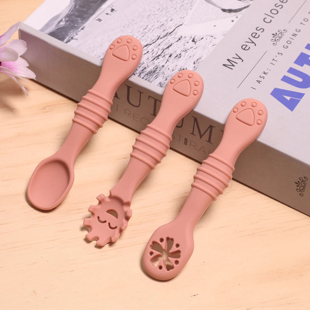 Three pink silicone spoons with unique designs on a wooden surface.