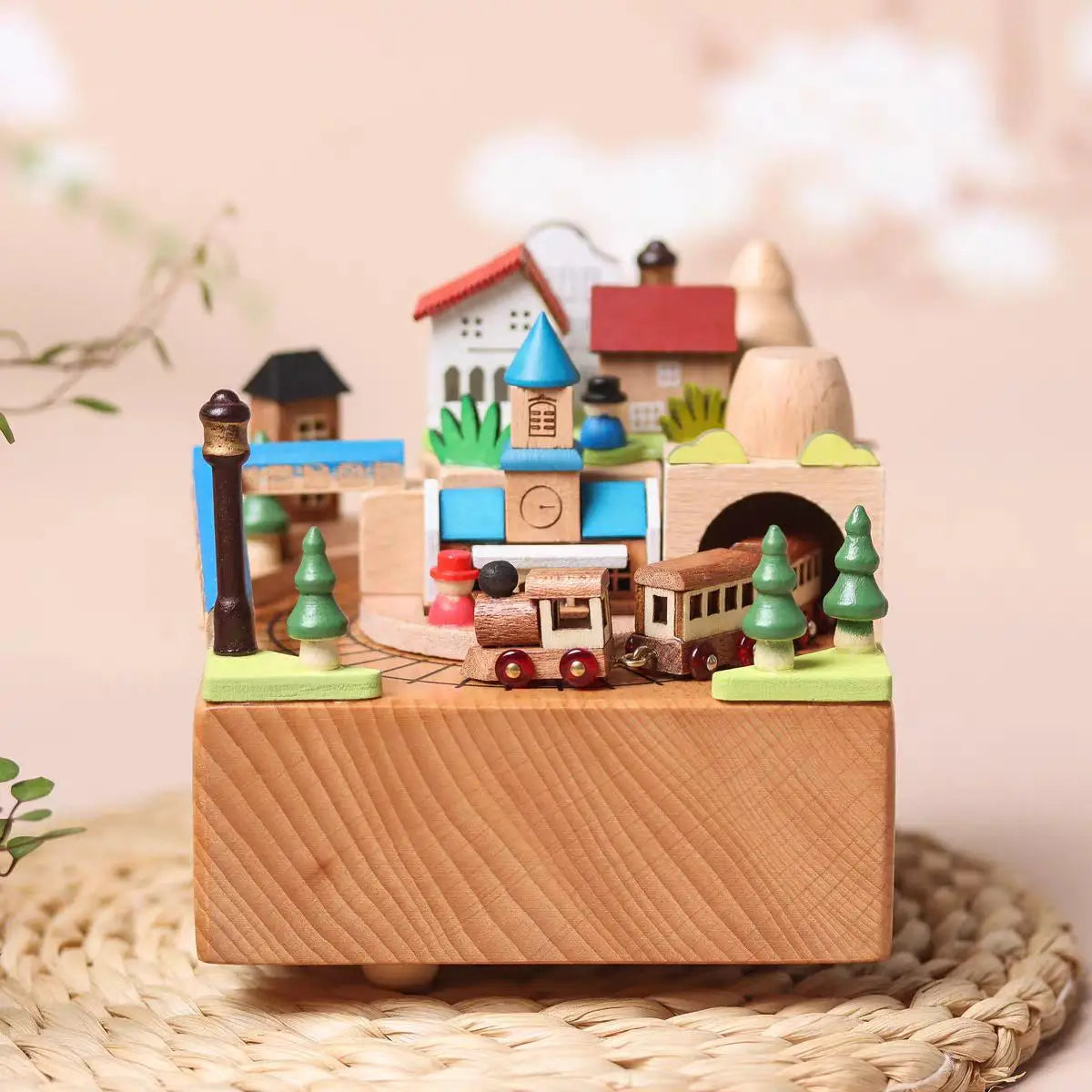 Wooden toy village with houses, trees, and a train on a woven surface.