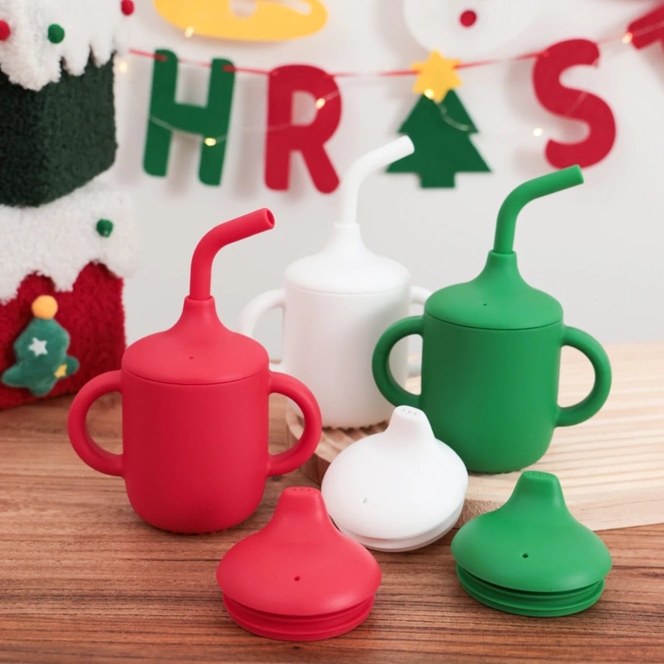 Red, white and green 2-in-1 silicone sippy and straw cups in front of a Christmas banner