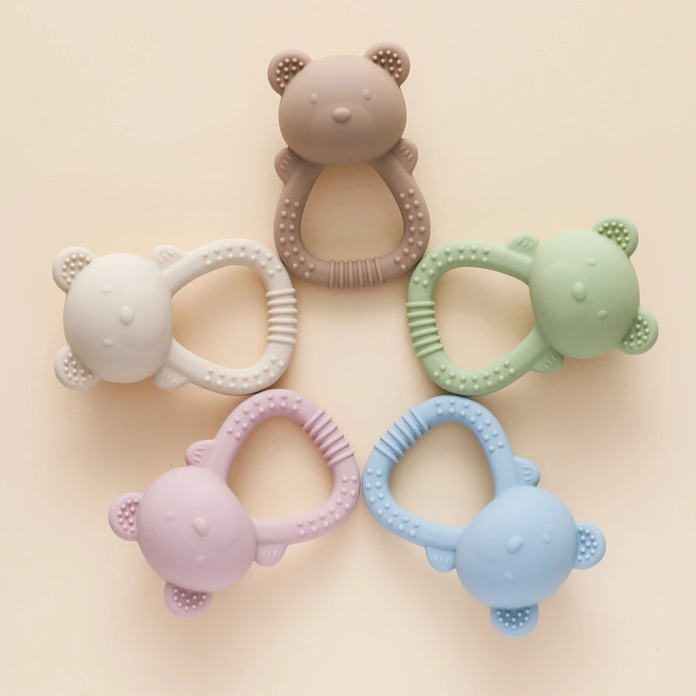 Set of five colorful bear-shaped teething rings on a beige background