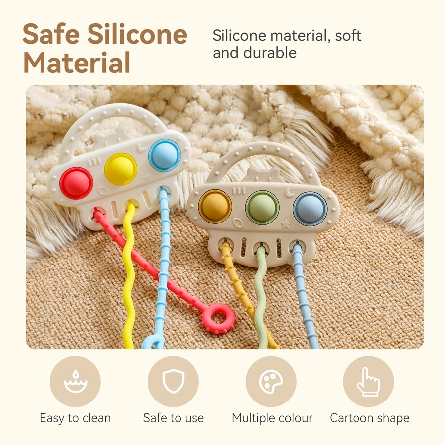 Two silicone baby sensory toys with colorful wavy cords and buttons, displayed on a textured beige rug with a cream knit blanket. The image includes marketing text highlighting 'Safe Silicone Material' and feature icons for 'Easy to clean', 'Safe to use', 'Multiple colour', and 'Cartoon shape'.