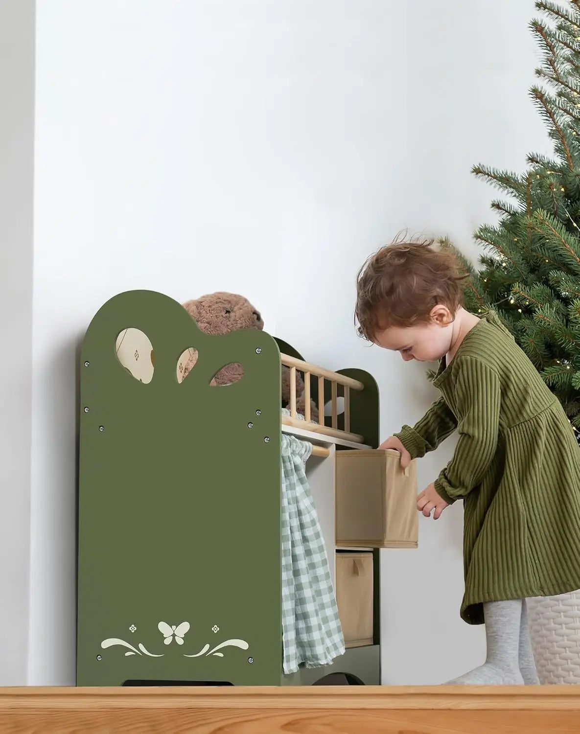 Child playing with a green toy wardrobe in a room with a Christmas tree.