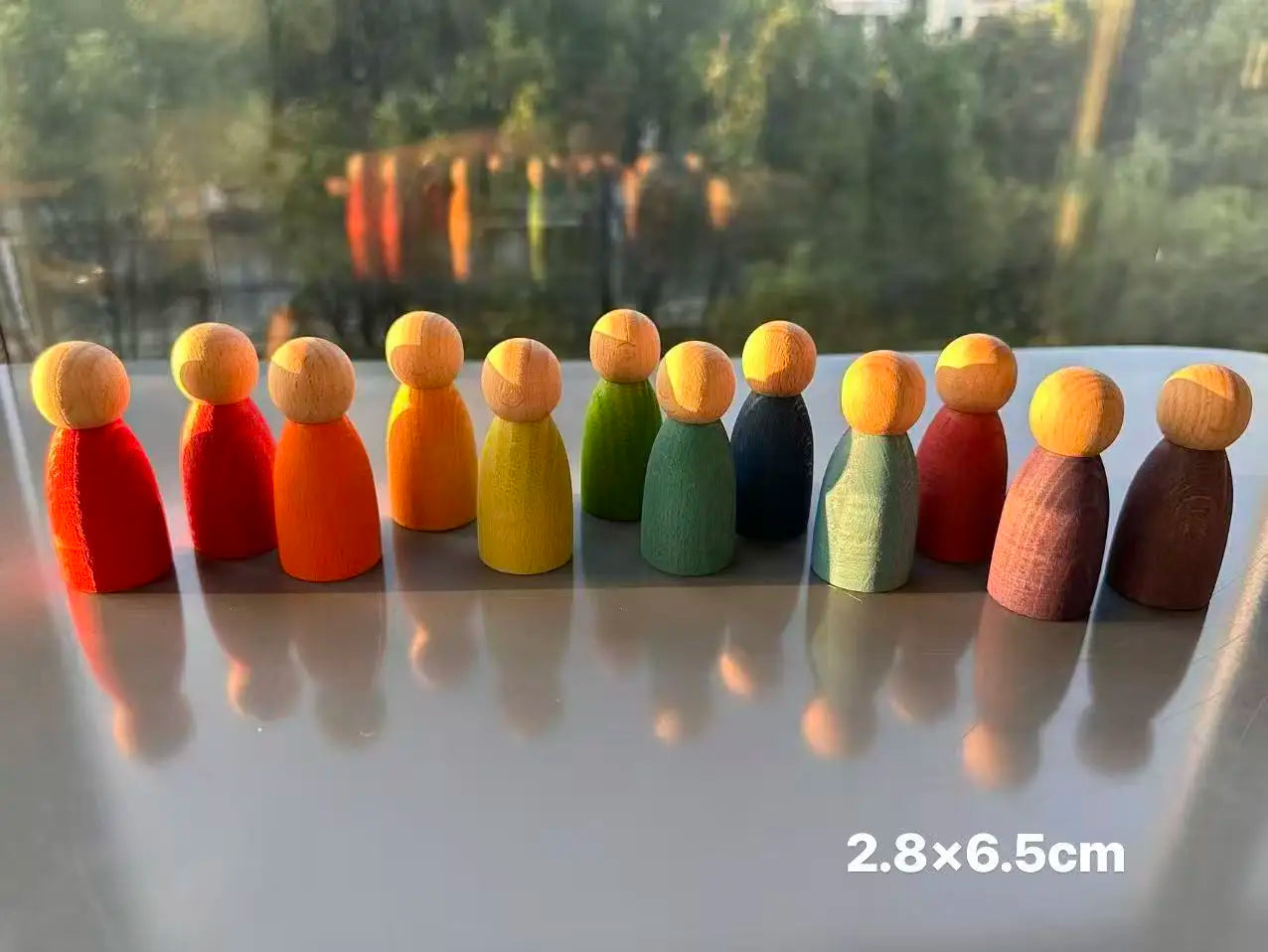 Row of colorful wooden peg dolls on a reflective surface with a blurred natural background