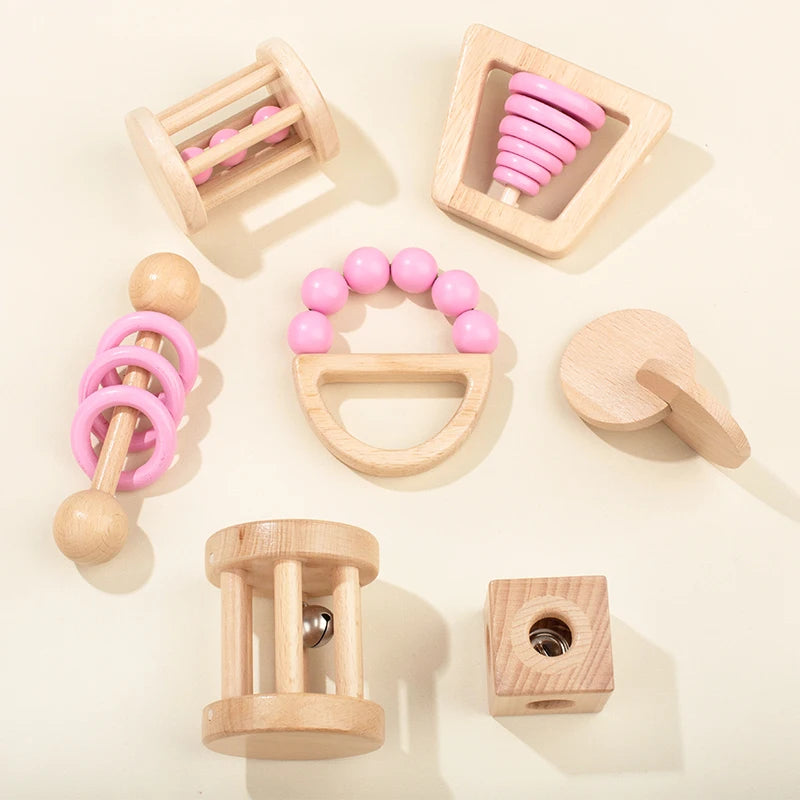 Collection of wooden baby toys with Montessori Wooden Baby Rattle Set with Soft Sensory Book | Oliver Montessori Toyspink accents on a light beige background