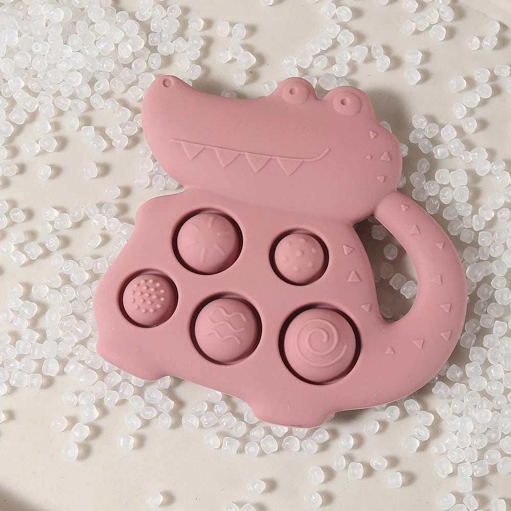 Pink crocodile-shaped teething toy with various textures on a textured beige background