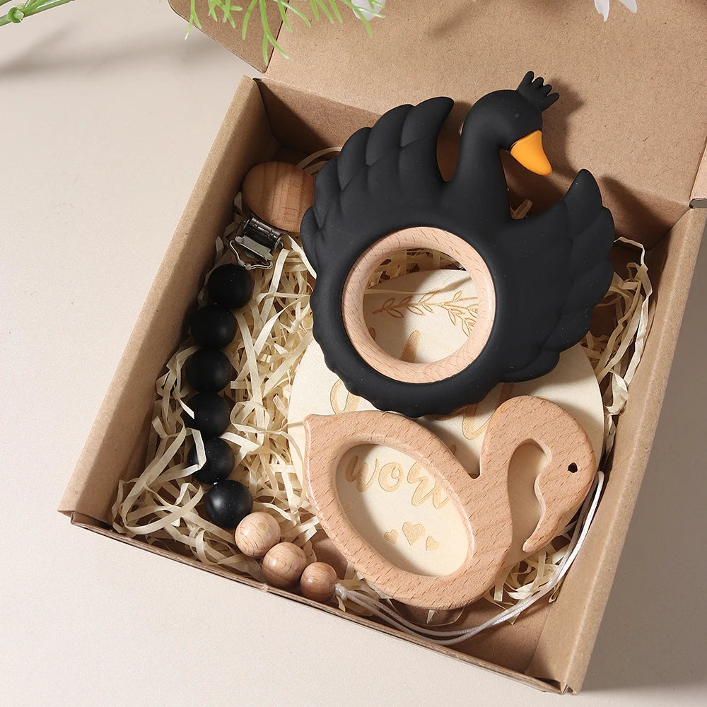 Set of baby teething toys including a black and wooden swan, wooden ball, and black keychain in a box.