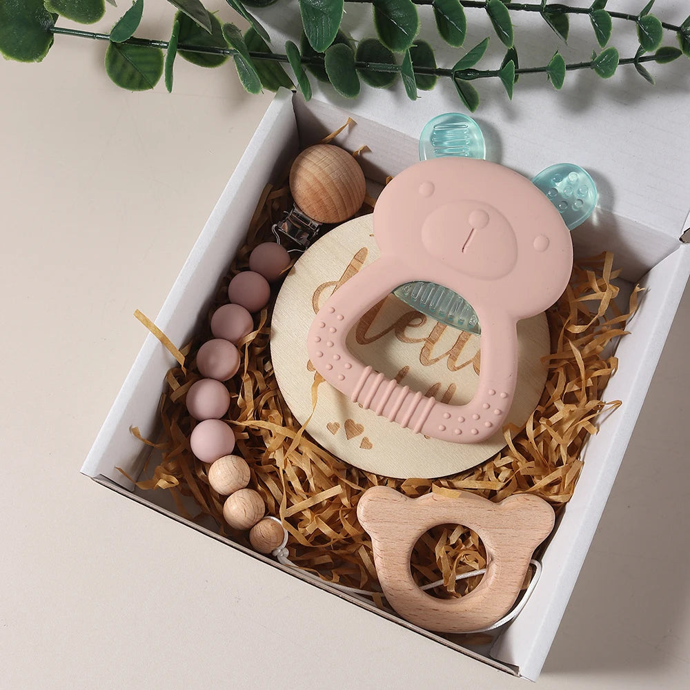Set of baby teething toys in a decorative box with greenery on a light background