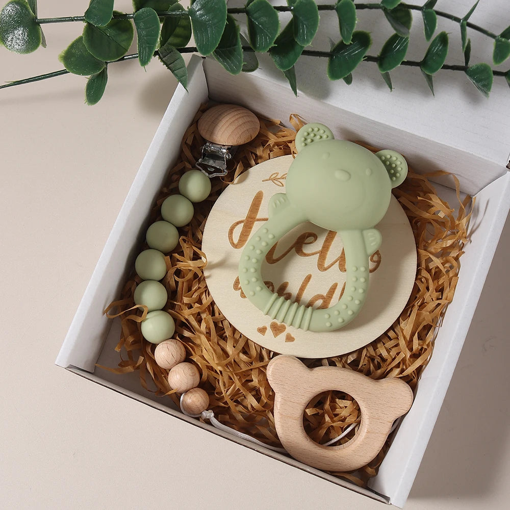 Baby teething ring set with green and wooden elements in a box with decorative plants.