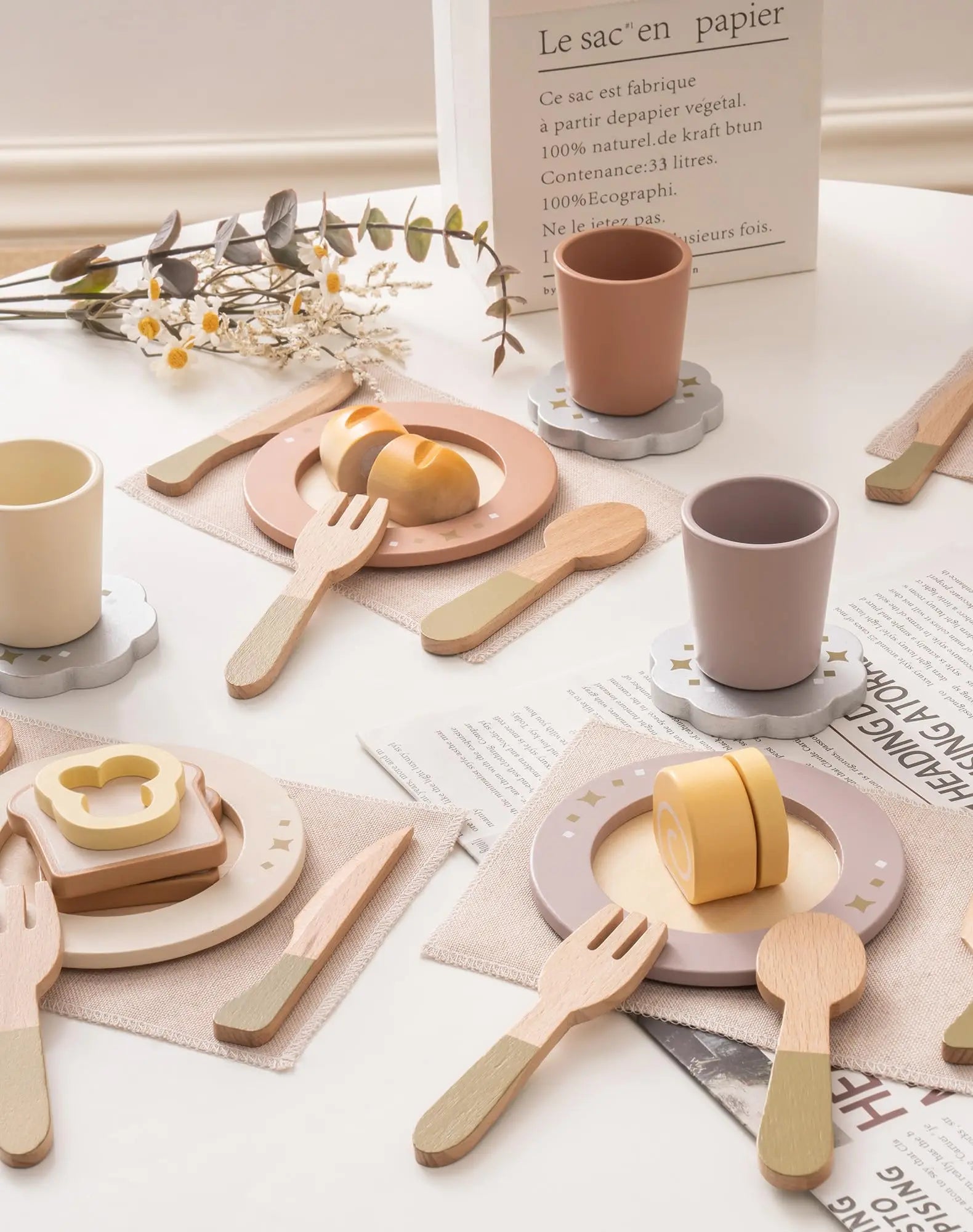 Set of wooden tableware including cups, plates, and utensils on a light surface with a newspaper.