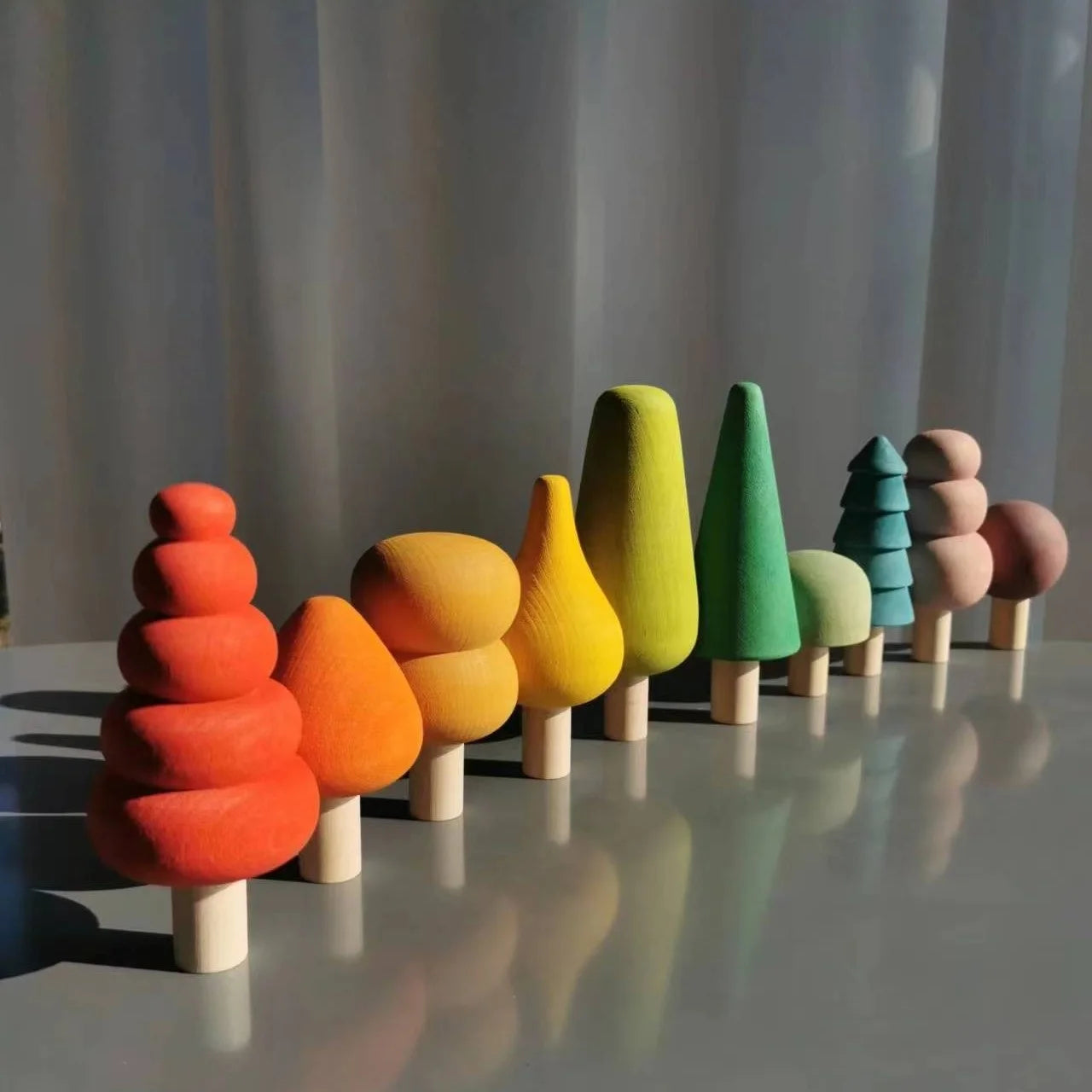Colorful wooden tree toys on a reflective surface with a neutral background