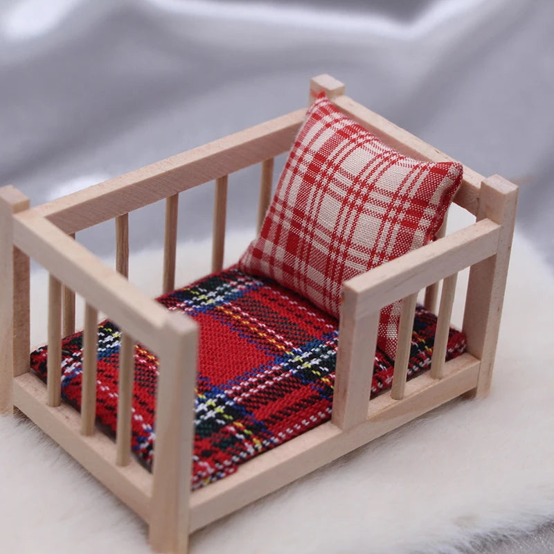 Miniature wooden crib with a red plaid blanket and pillow on a neutral background