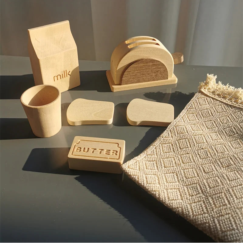 Set of wooden kitchen items including a milk carton, toaster, and butter block on a gray surface with a textured fabric background.