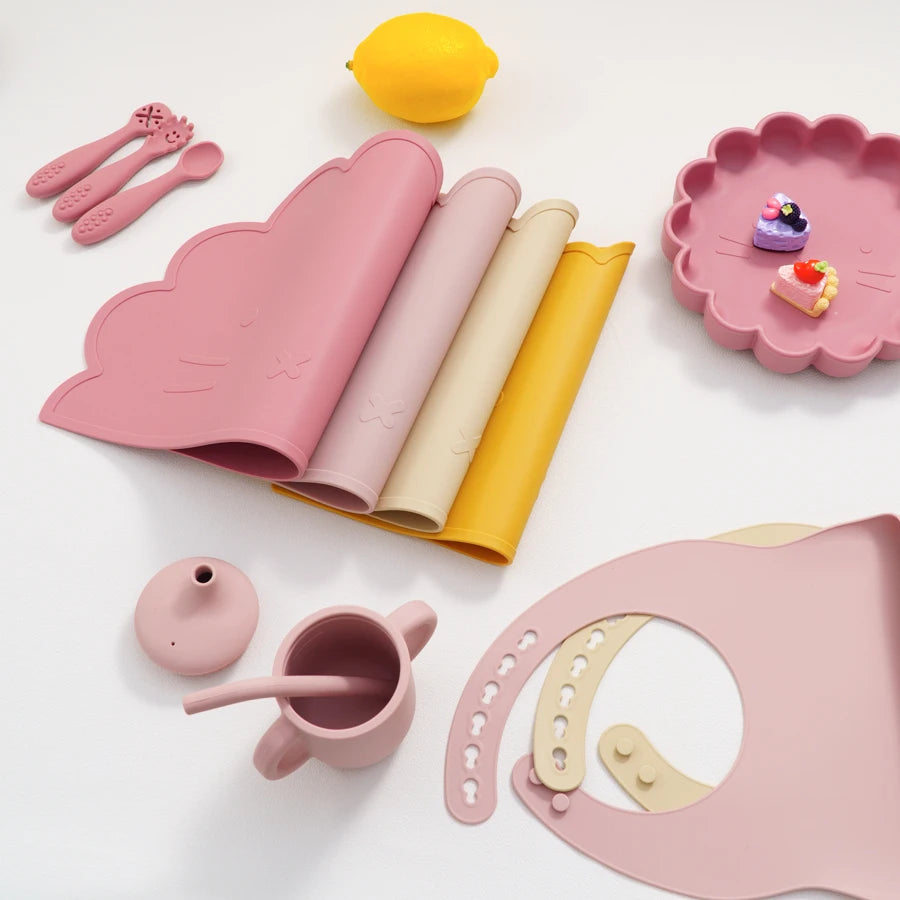 Collection of pink children's tableware including mugs, spoons, and plates on a white background.