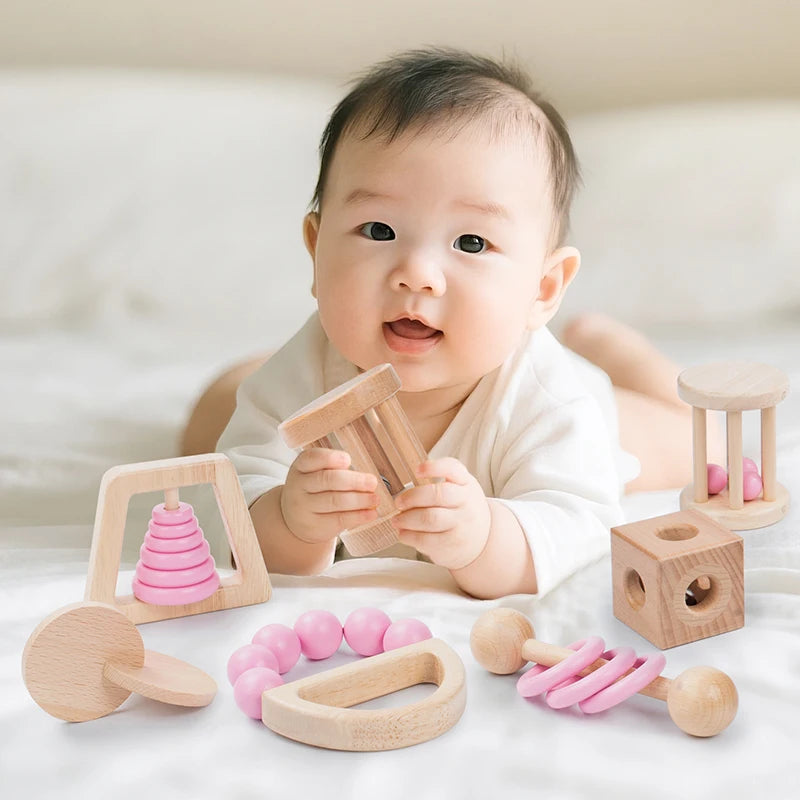Baby playing with wooden toys on a white surface. Montessori Wooden Baby Rattle Set with Soft Sensory Book | Oliver Montessori Toys